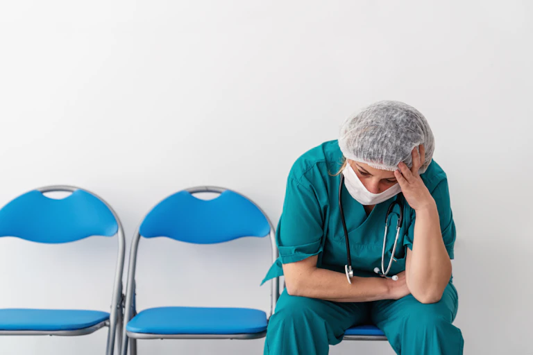 A doctor in scrubs with her head in her hands