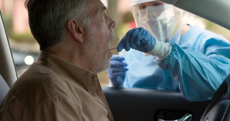 A man being a swab test while sitting in his car.