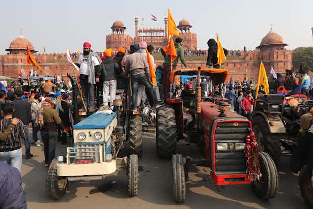 Men with flags stand on two tractors overlooking Delhi's Red Fort