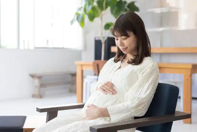 A pregnant woman sitting on a chair holding her bump.