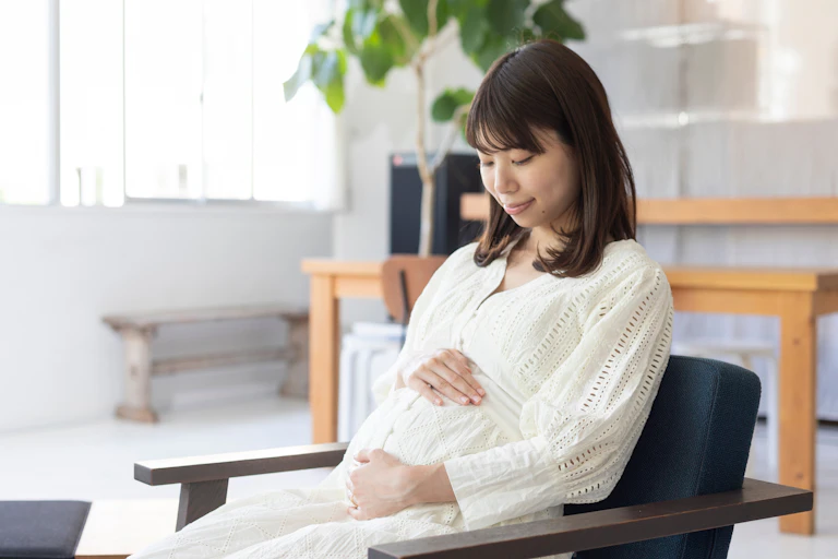 A pregnant woman sitting on a chair holding her bump.