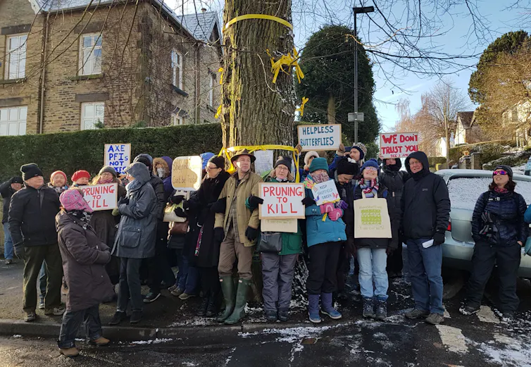 Protesters hold signs including 'pruning to kill'