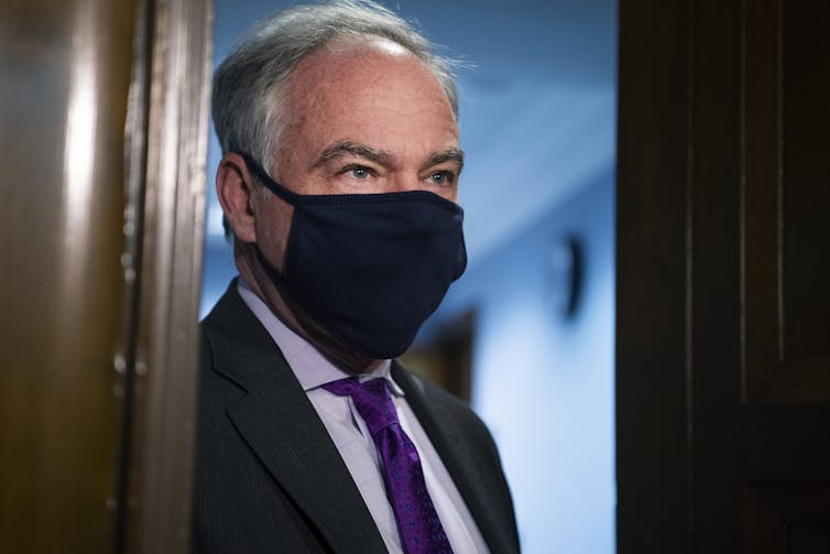 Kaine stands in a doorway wearing a face mask