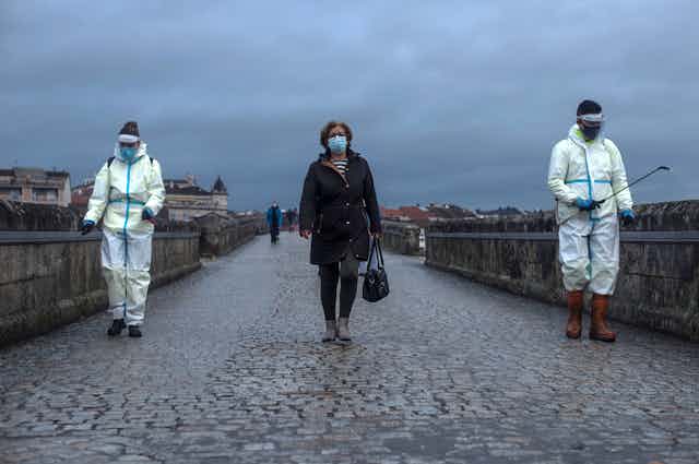 A woman crosses the Roman Bridge in Galicia, Spain, as local workers disinfect it