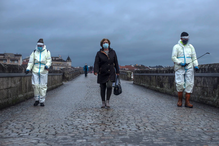 A woman crosses the Roman Bridge in Galicia, Spain, as local workers disinfect it
