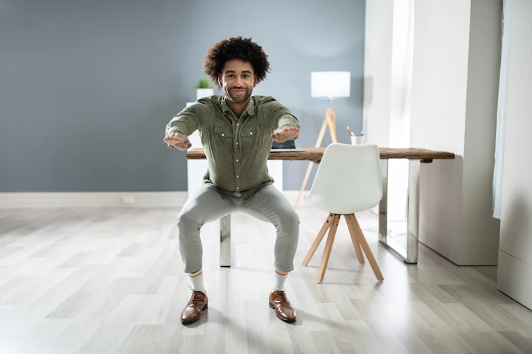 A man doing squats next to his desk