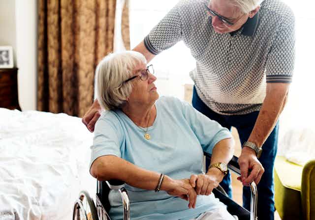 An older man helping an older woman use a wheelchair