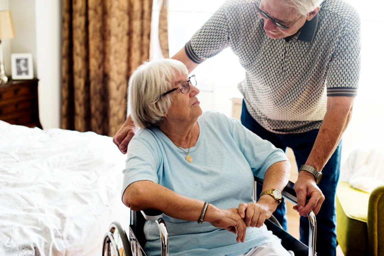 An older man helping an older woman use a wheelchair