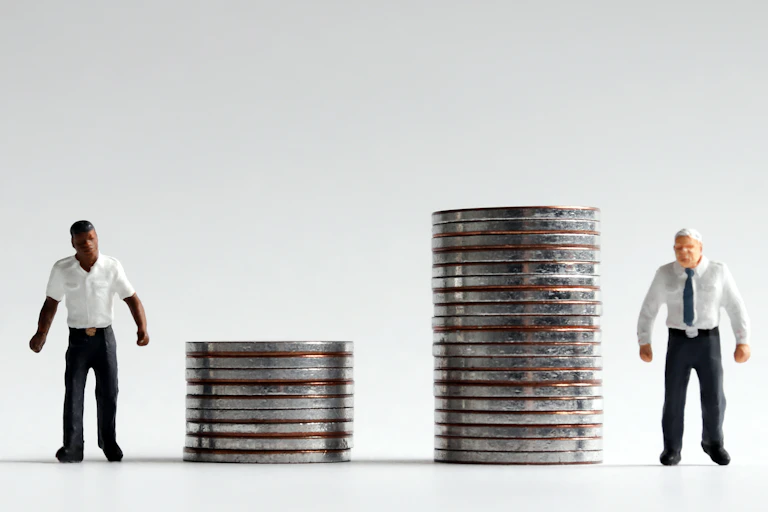 Black man standing nexts to a short stack of quarters and a white man stands next to a tall stack.