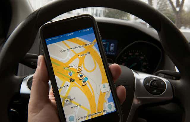 A hand holds an iPhone displaying the Waze traffic app. 