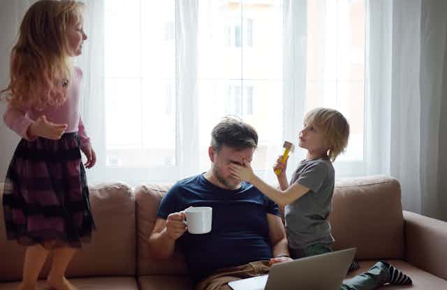 Kids play around a father on a couch.