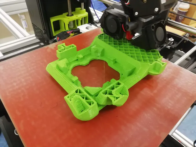 A green chassis for a robot is 3D printed in a scientists' lab