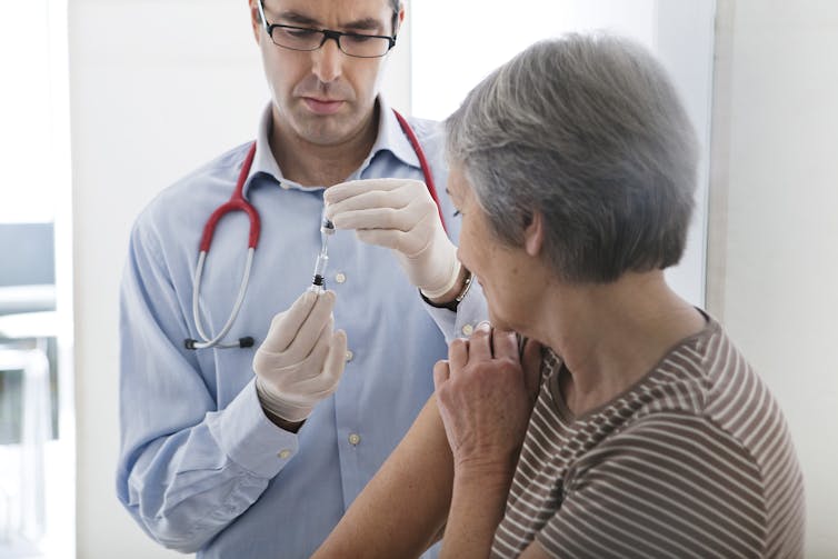A doctor prepares to vaccinate a grey-haired woman.