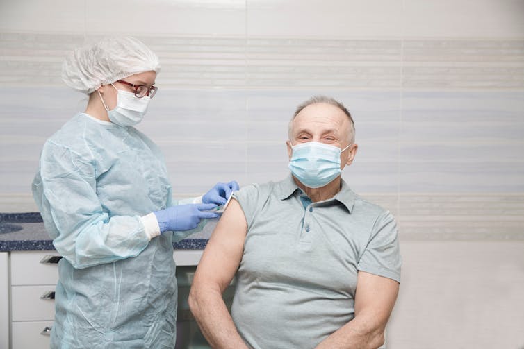 A health-care worker administers a vaccine to a senior man.