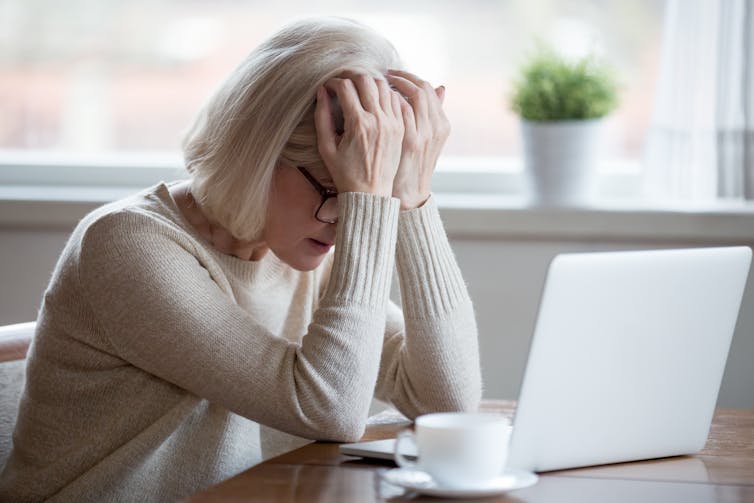 woman with head in hands is distressed by what she has just read on her laptop