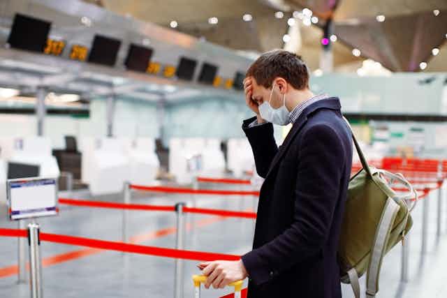 Man in mask, puts his head in hand at empty airport check-in