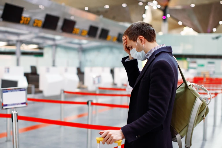 Man in mask, puts his head in hand at empty airport check-in