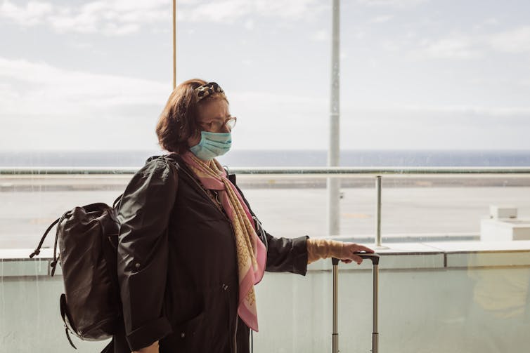Elderly woman in mask waits at airport.