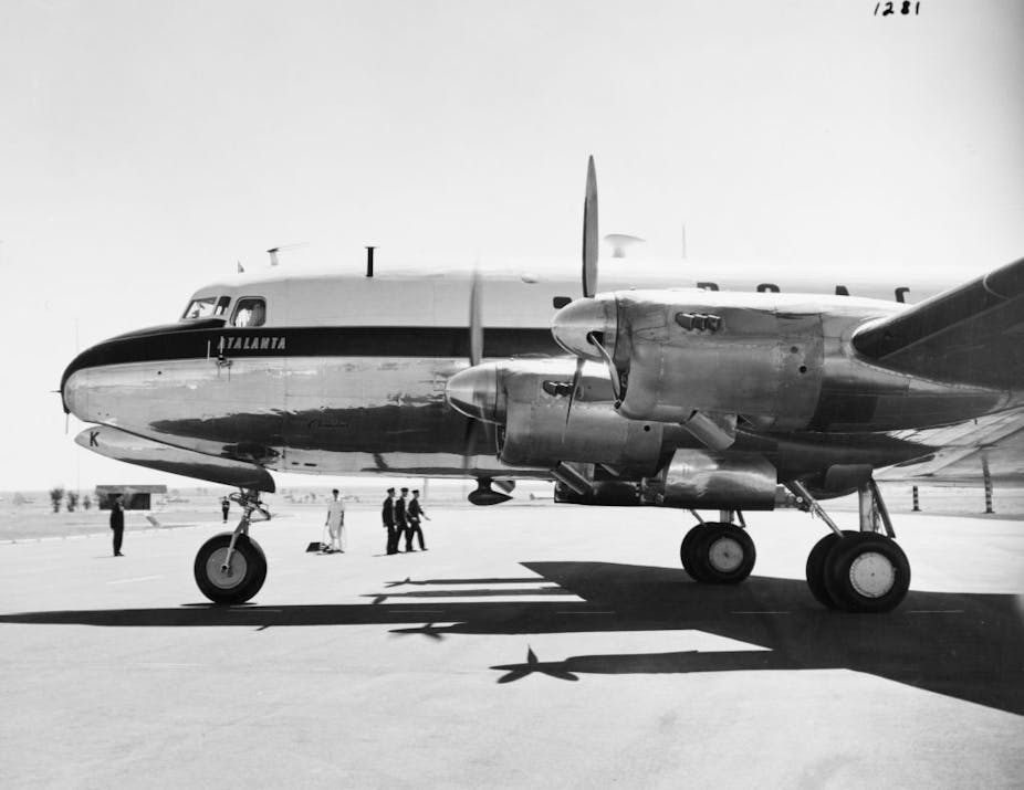 An 1950s aeroplane stands on the tarmac with British colonial servicemen in the background.
