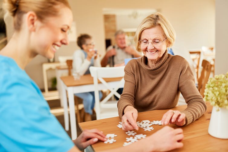 Elderly woman and her nurse completing a puzzle in a care home.