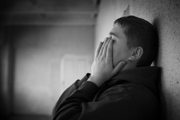 Black and white photo of teenager with head in his hands