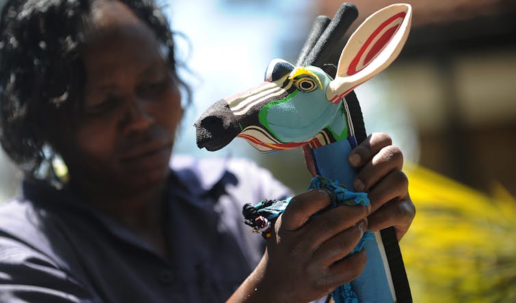 A woman concentrates as she works on a brightly coloured giraffe curio, constructed in layers of plastic.