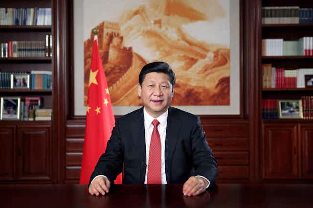 Chinese president Xi Jinping delivers speech from his desk in front of a painting of the Great Wall of China and the national flag.