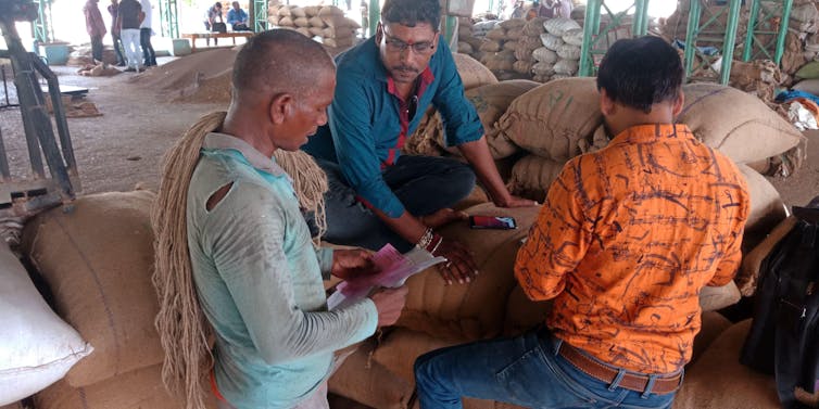 Three farmers make a deal around agricultural sacks in an Indian mandi
