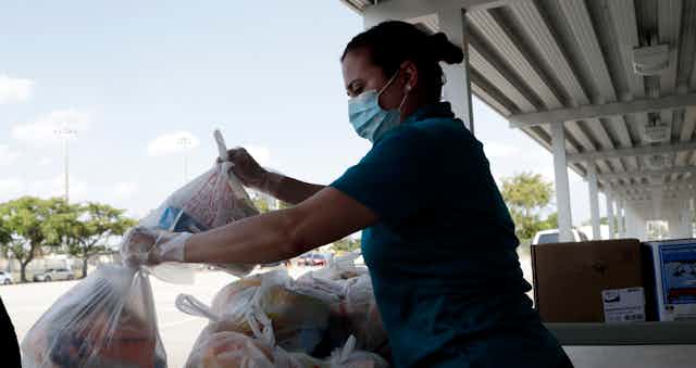 A woman wearing a mask holds plastic bags to give away.