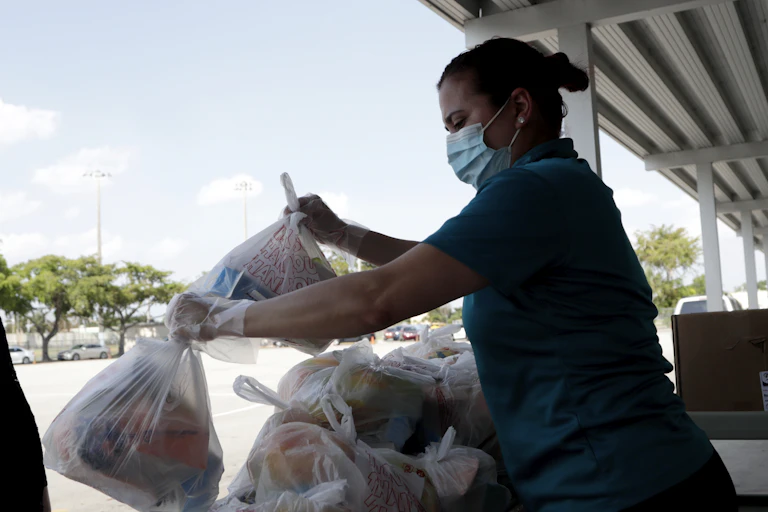 A woman wearing a mask holds plastic bags to give away.