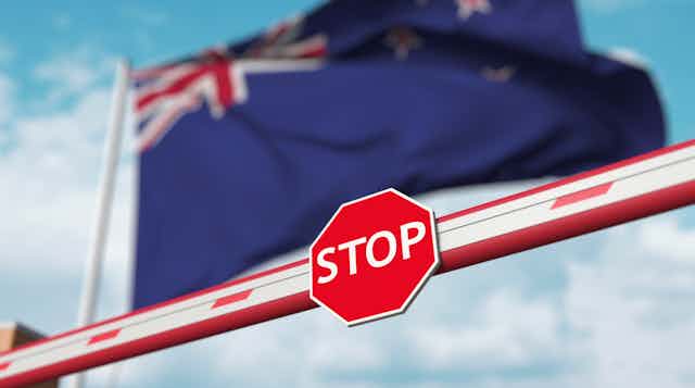 A stop sign on a barrier in front of a New Zealand flag.