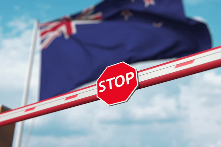 A stop sign on a barrier in front of a New Zealand flag.