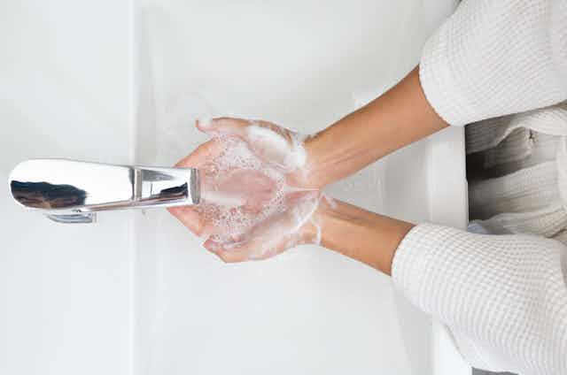 Vista cenital de una persona aclarándose las manos enjabonadas en un lavabo.