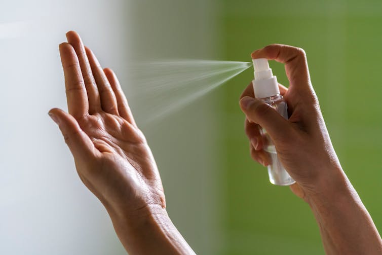 Una persona pulveriza sobre una de sus manos un gel hidroalcohólico.