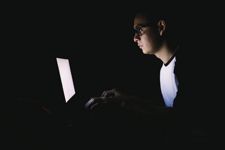 Young man working on his laptop in the dark.