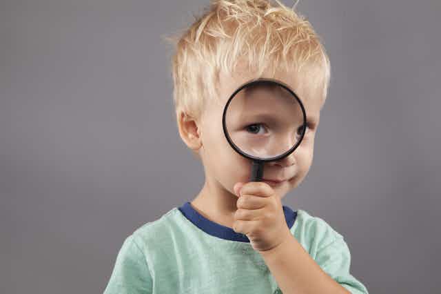A young boy holds a magnifying glass up to his eye