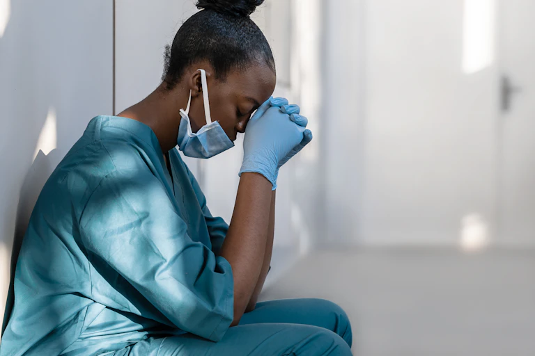 A woman in scrubs sat with her head in her hands.