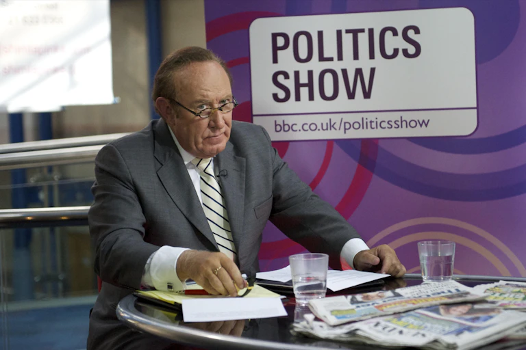 BBC politics broadcaster Andrew Neil sitting at a desk covered in newspapers in front of a sign saying: Politics Show.