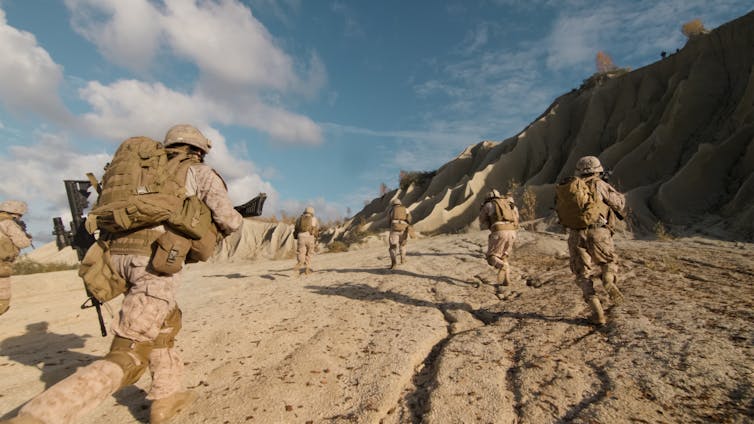 Squad of soldiers running with guns in a desert