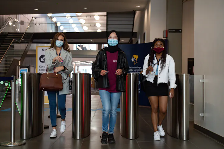 Three university students walk through an electronic barrier.
