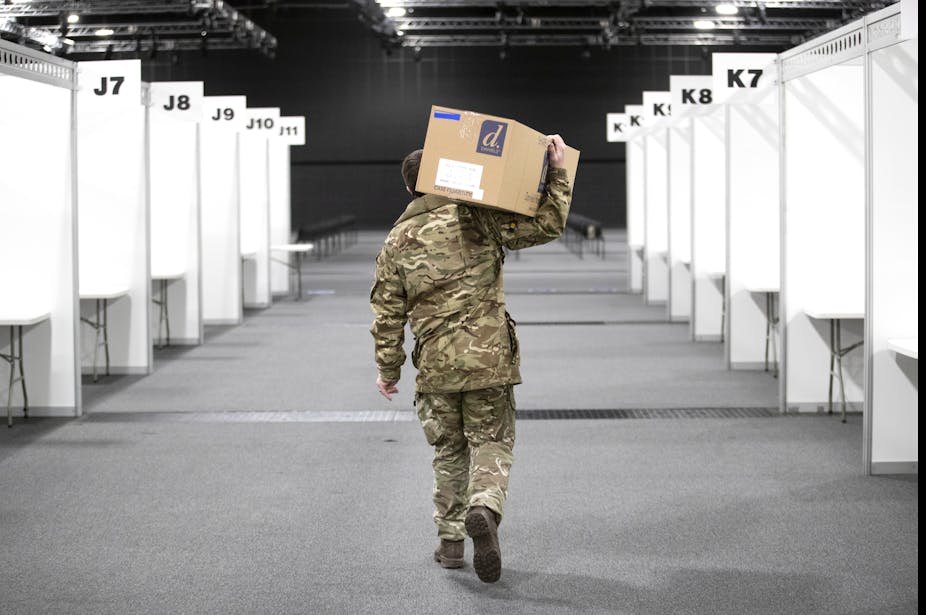 A man in army fatigues carries a box through a vaccination centre