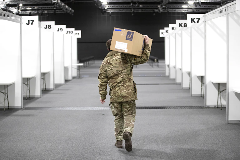 A man in army fatigues carries a box through a vaccination centre