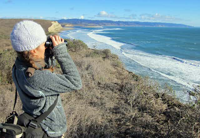 Woman with binoculars on seaside cliff