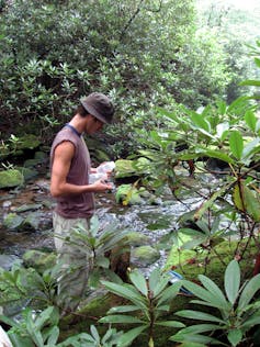 Man holding plastic bottles stands in stream.