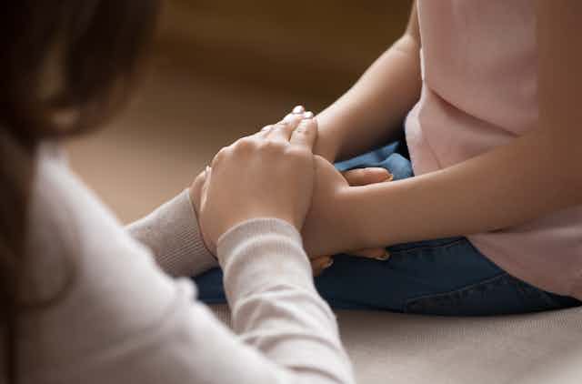 An adult clasps a child's hand in hers