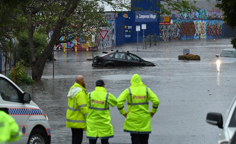 Emergency staff look on as cars and houses are flooded.