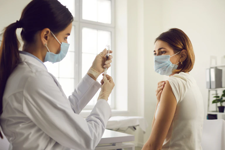 A nurse in a face mask preparing to vaccinate a woman in a face mask
