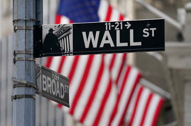 A Wall Street street sign with the American flag in the background.