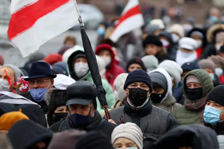 Crowded street full of protesters wearing masks and carrying flags of the Belarus protest movement.