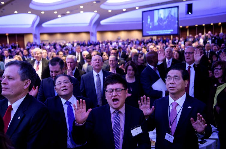 A crowd of hundreds of mostly older people stand singing and praying